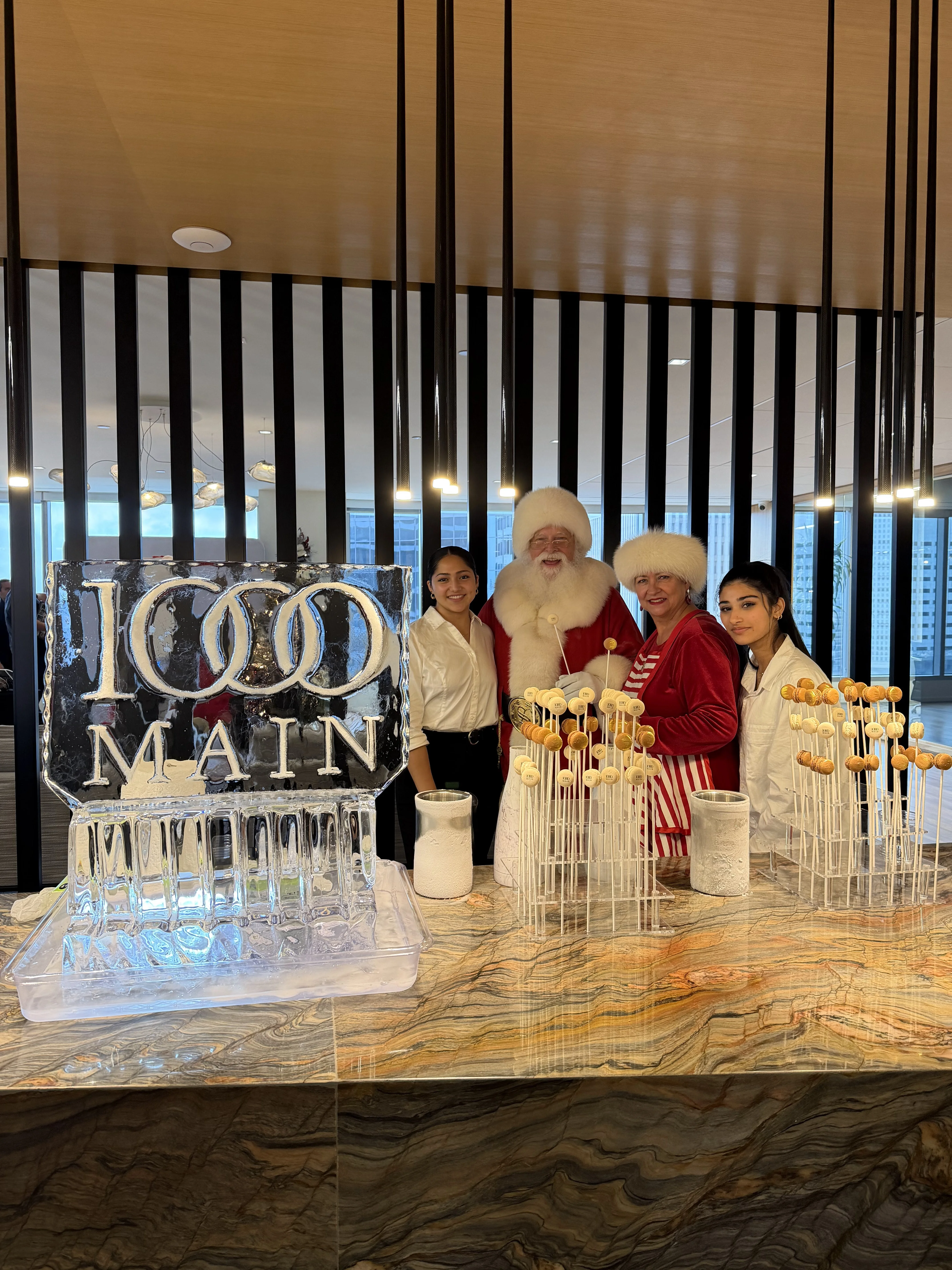 Corporate holiday party ice cream catering in Houston: Santa, Mrs. Claus and Freezing Point servers behind NitroPop Macarons on sticks beside a logo ice sculpture in an office tower lobby