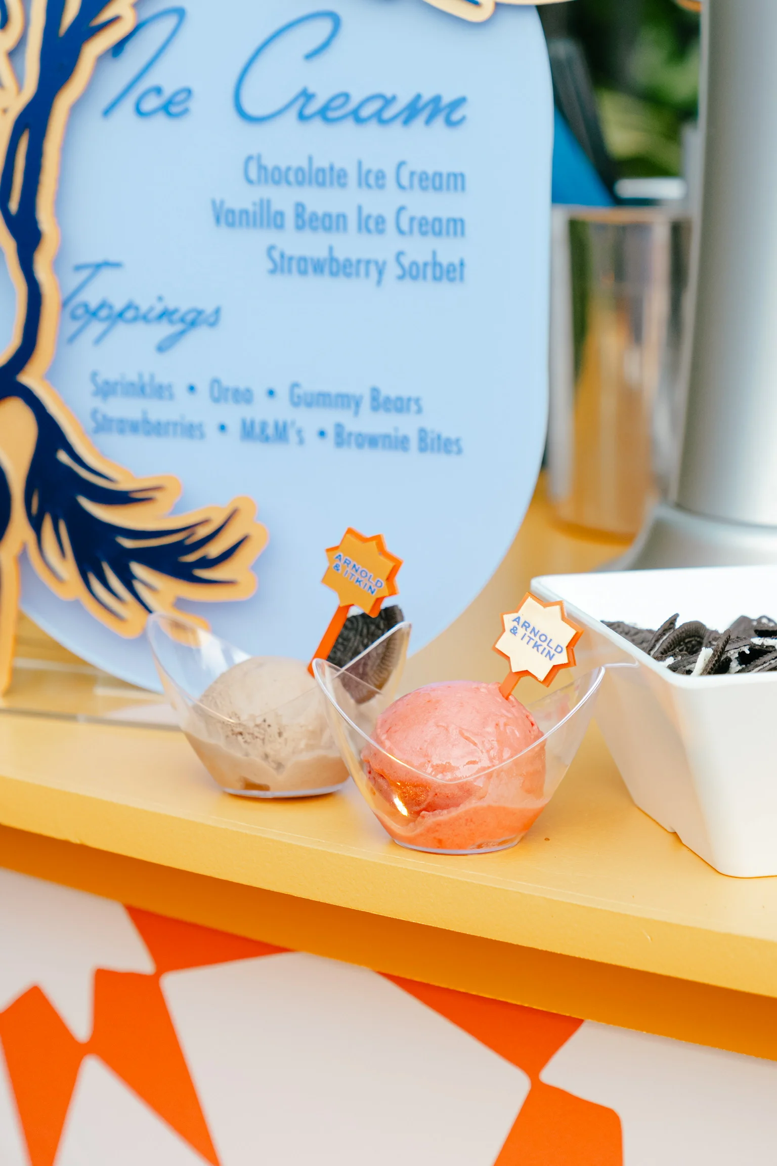 Employee appreciation ice cream catering: chocolate ice cream and strawberry sorbet with custom company-logo picks beside a branded ice cream and toppings menu